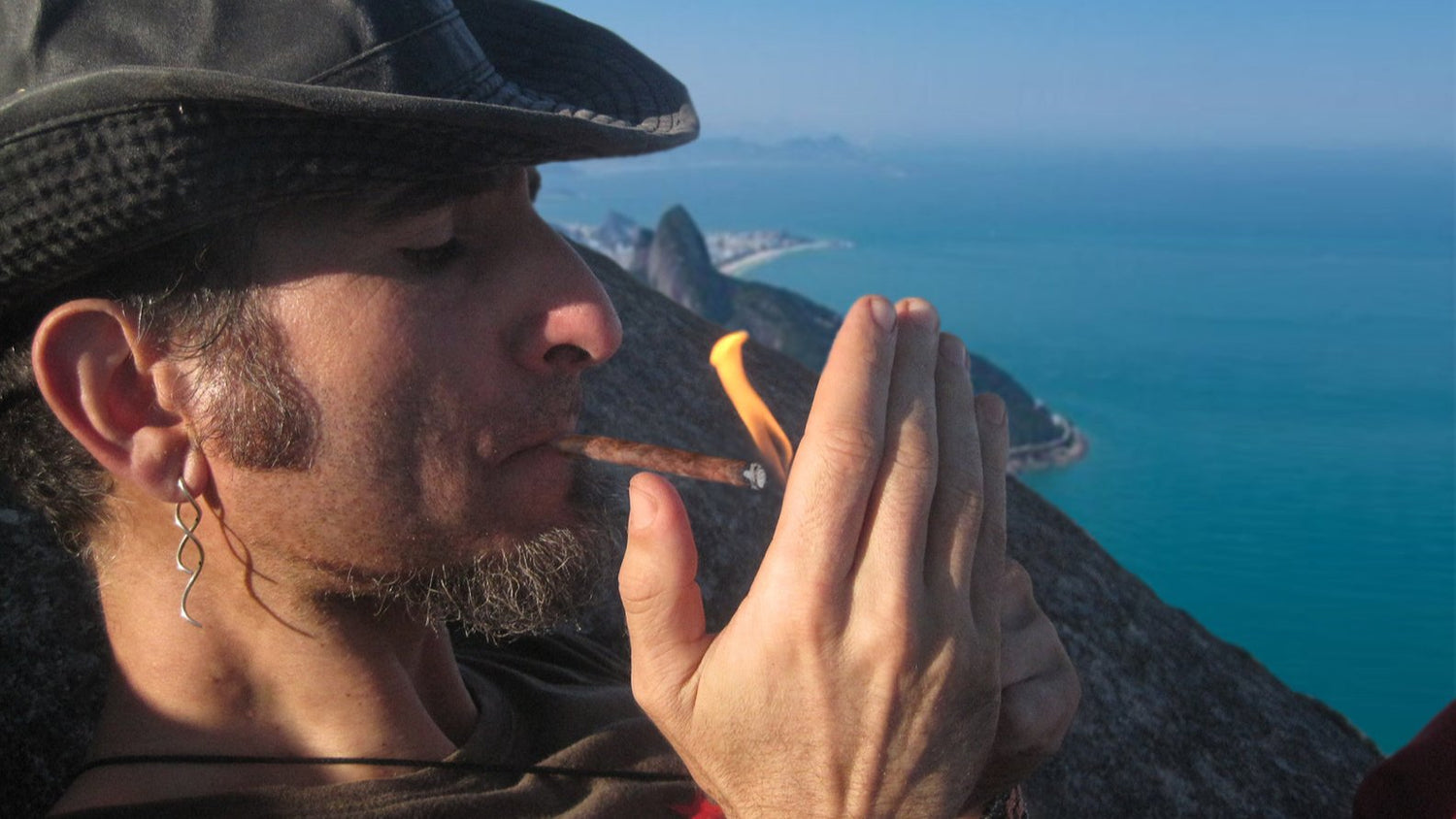 Person lighting a cigarette with coastal view in the background